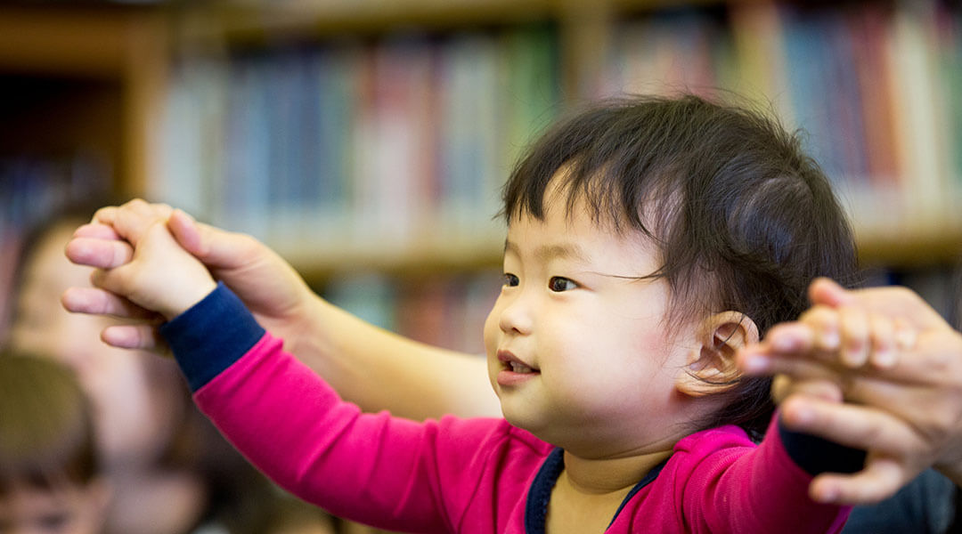 A caregiver helps a baby do hand gestures to accompany a rhyme.