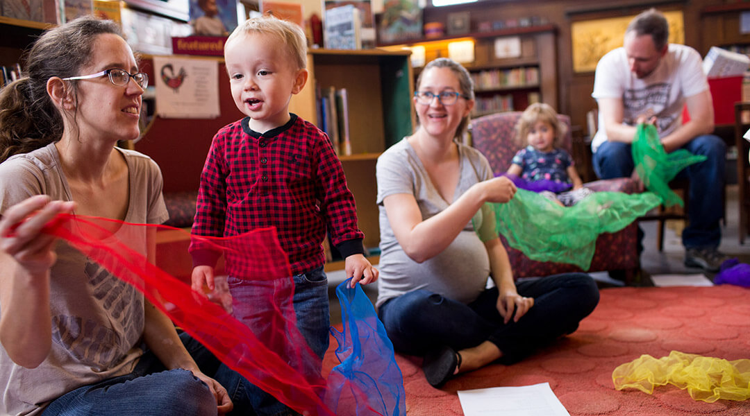 Babies and their caregivers play with scarves during storytime.