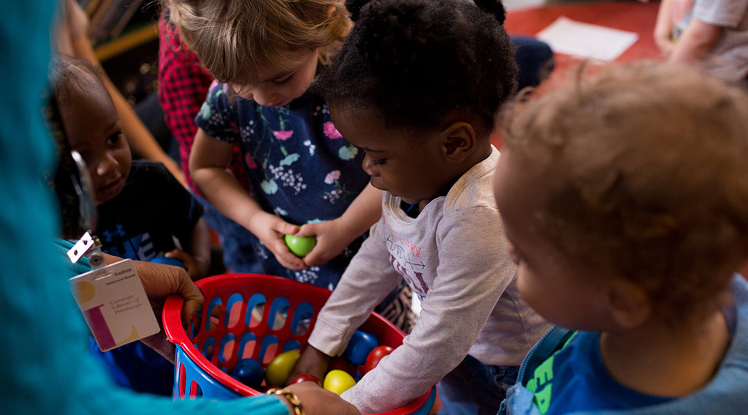 Three small children look through a basket of shaker eggs the librarian offers them.