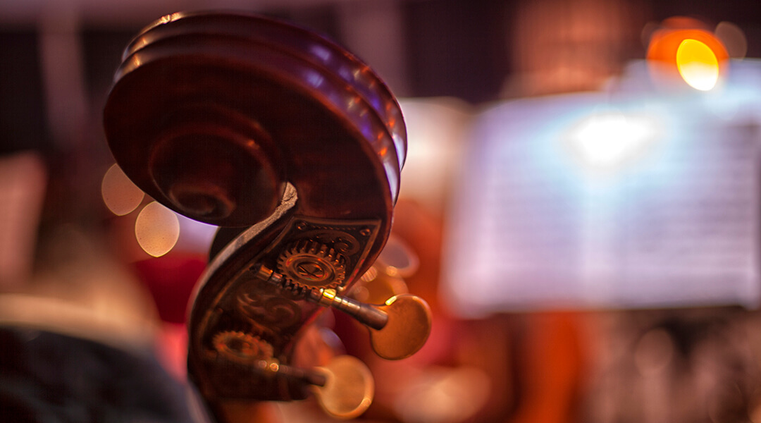 The curve of a cello with sheet music out of focus in the background.