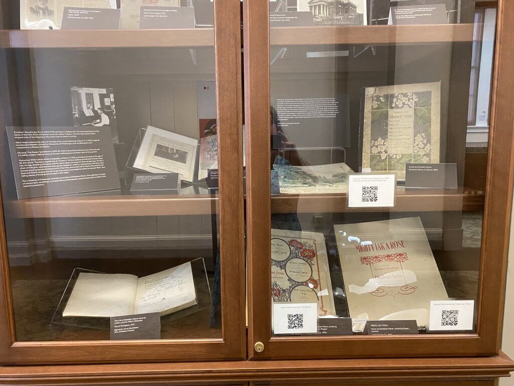 Glass and wood exhibit case featuring sheet music covers and signatures on books