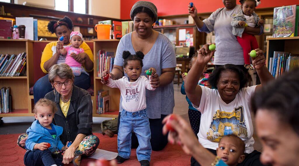 Parents and caregivers dance with small children during storytime.