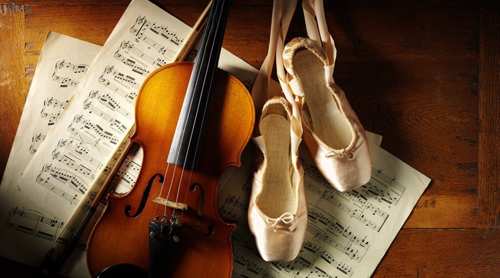 Wooden violin on sheet music with a pair of ballet shoes on a old wooden background.