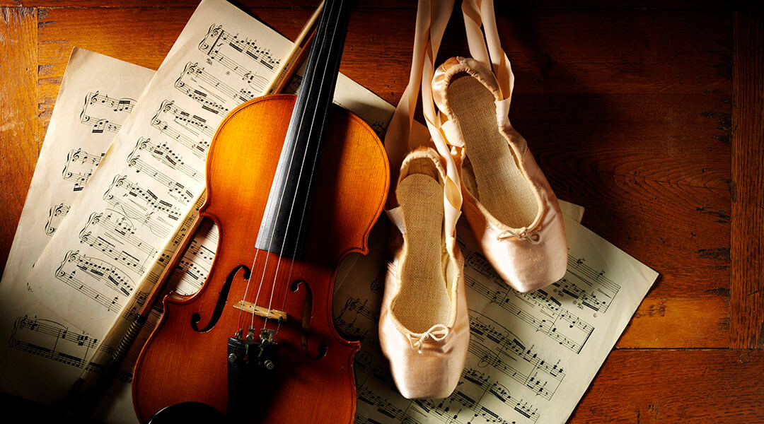 Wooden violin on sheet music with a pair of ballet shoes on a old wooden background.