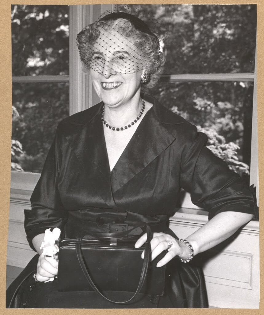 Black and white photo of a smiling middle aged white woman in a hat with a fancy net