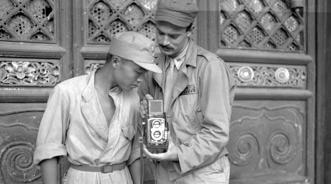 Black and white photograph from Historic Pittsburgh - Harold Corsini Photographs collection of young man, Harold Corsini, showing a local soldier his camera.