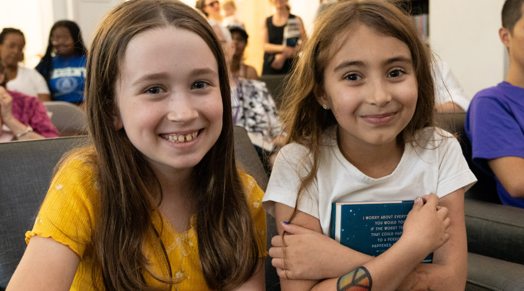 Two young girls smiling and hugging books at an author talk