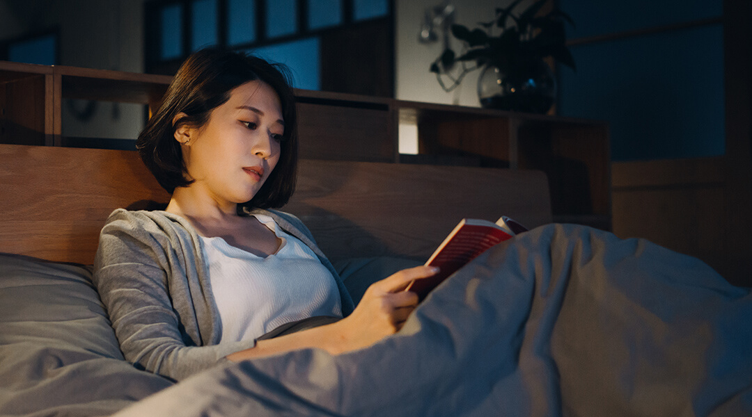 Relaxed adult lying in bed and reading a book at night