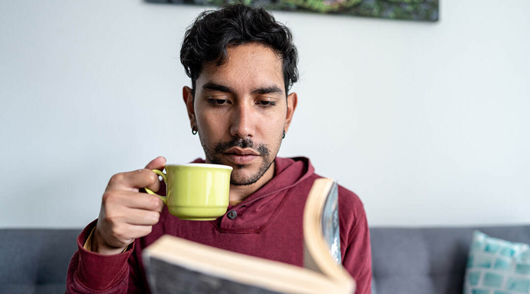 Young adult reading a book and drinking coffee at home