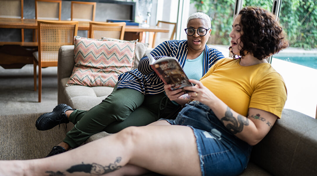Two adults talking and reading a book at home.