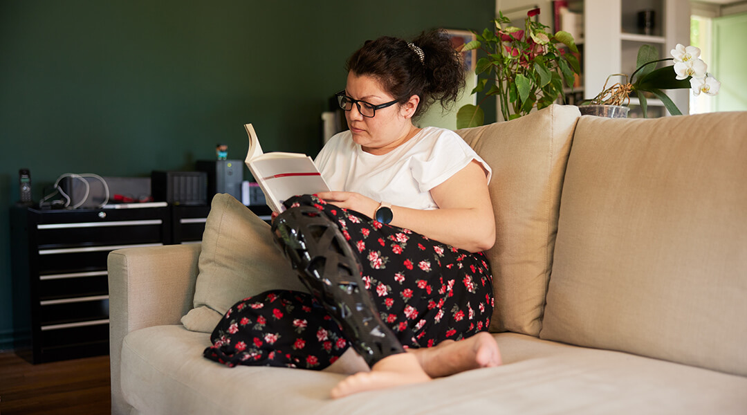 A woman with a prosthetic leg sits on a sofa reading a book.