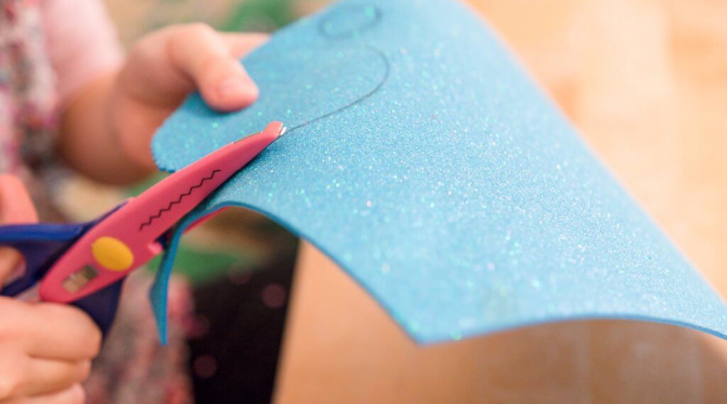 Close-up of a child using zig-zag scissors to cut a thin piece of foam.