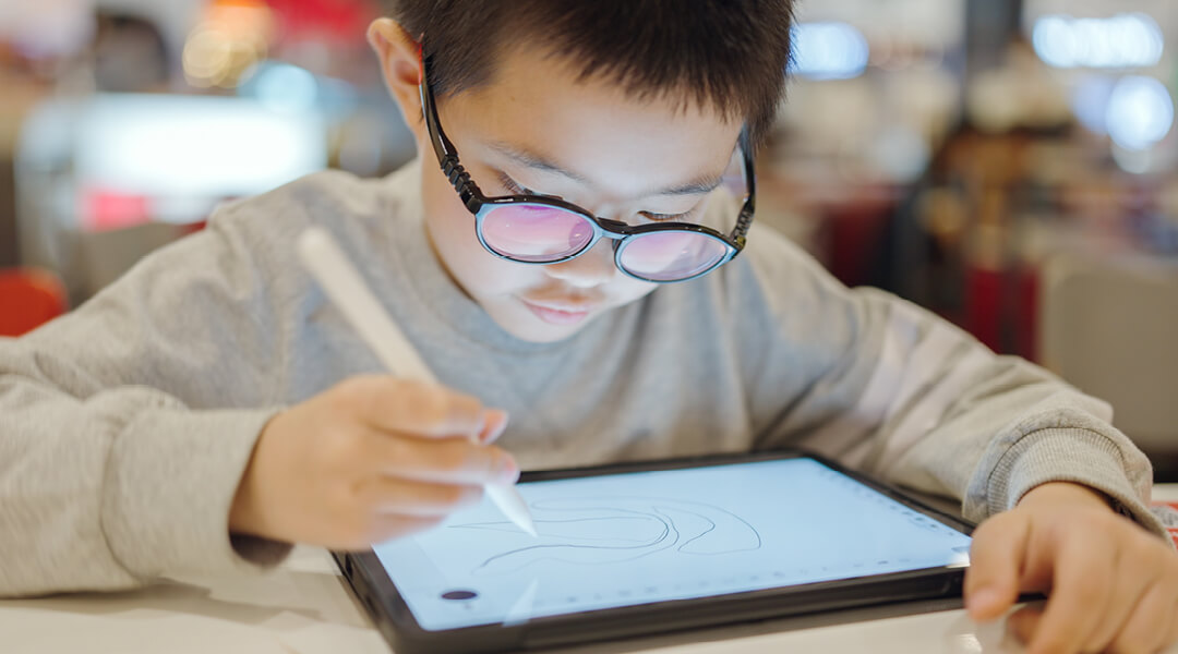 A young child draws on an iPad with a stylus.