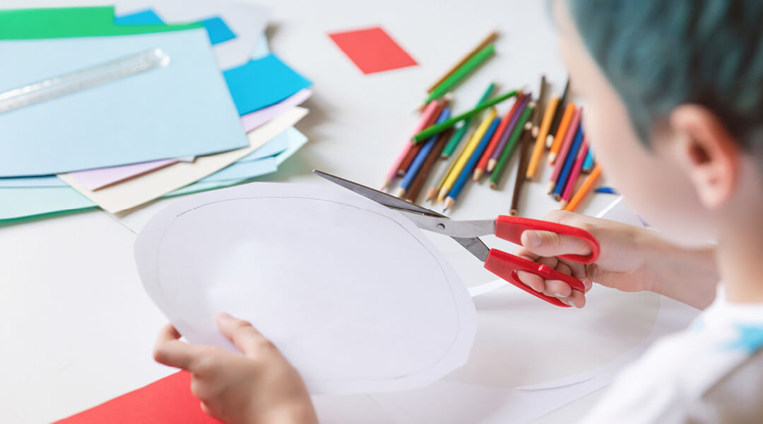A child cuts a piece of paper in the shape of a circle.