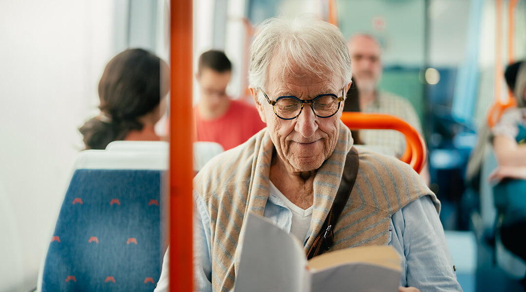 Senior adult reading book while traveling on a public bus.