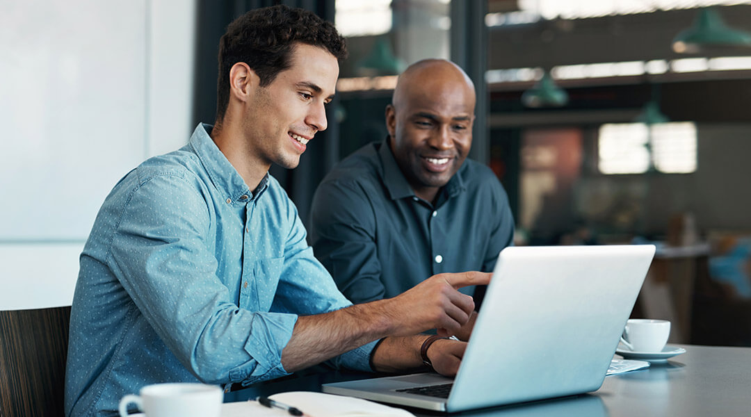 Two adults review work on a laptop together in an office setting.