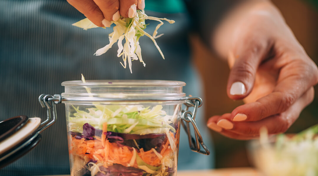 Close up of a hand dropping shredded cabbage and other vegetables into a jar for fermentation.