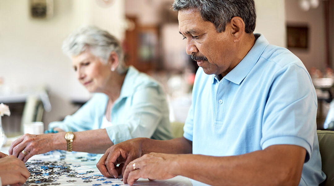 Two senior adults work on puzzles together in a shared lounge.