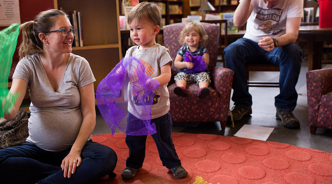 Two small children play with scarves during storytime with their caregivers.
