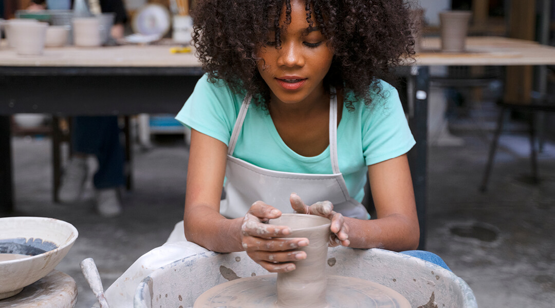 A teenager throws clay at a pottery wheel.