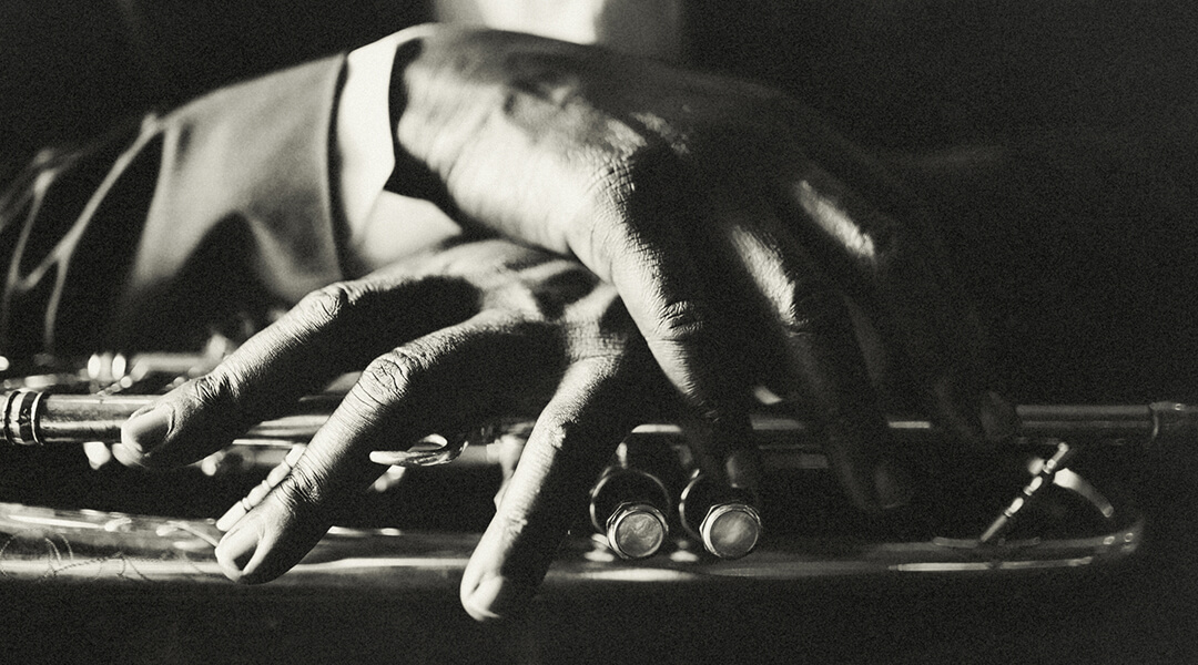 Close up of a pair of hands of a dark-skinned person, draped over a trumpet
