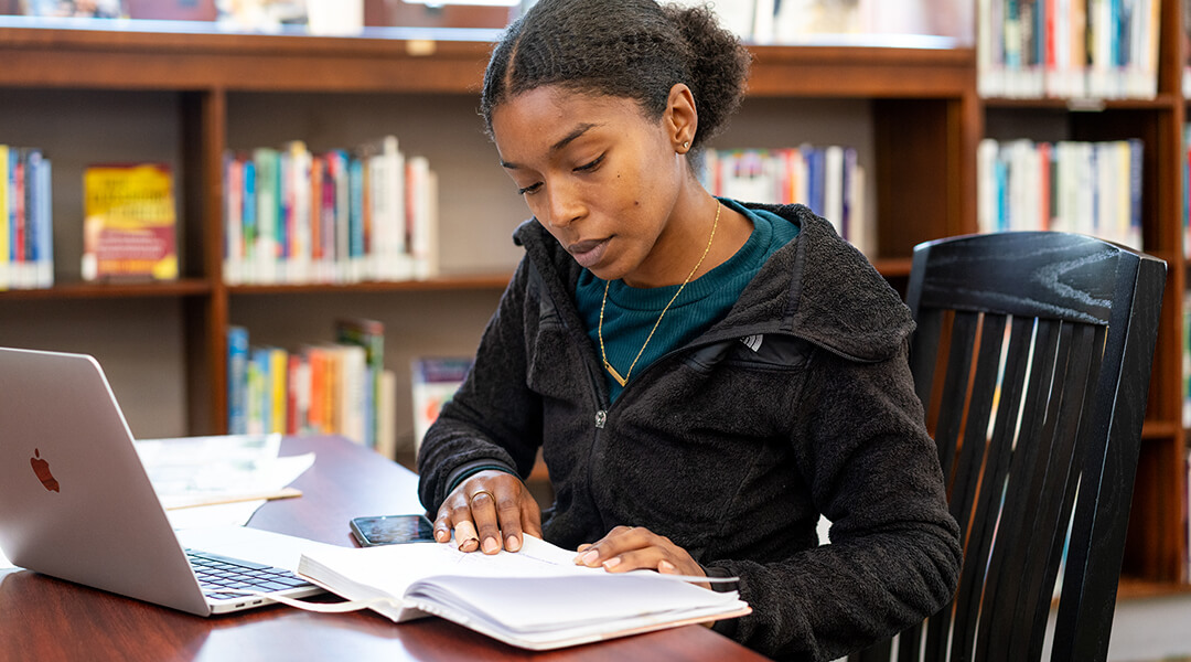 Woman sitting at library table with notebook and laptop