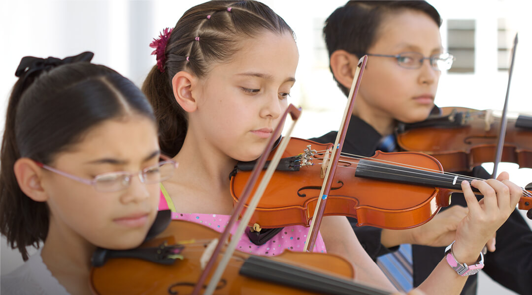 Three children standing in a line playing violin.