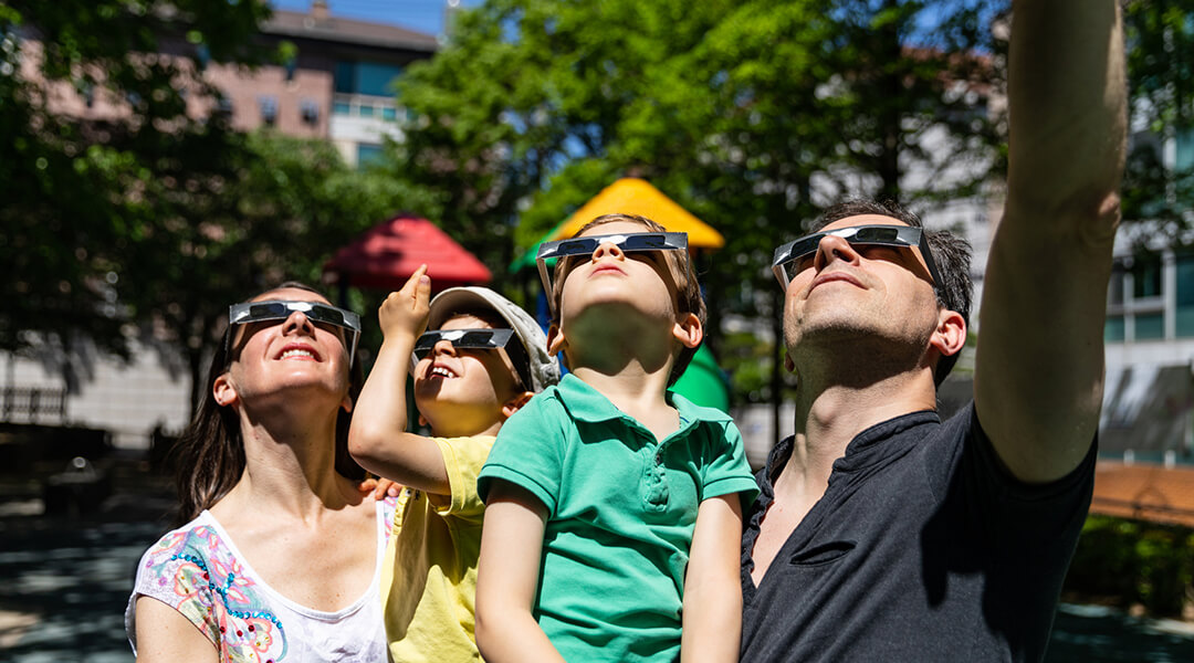 A family of four looking at solar eclipse with special glasses in a public park