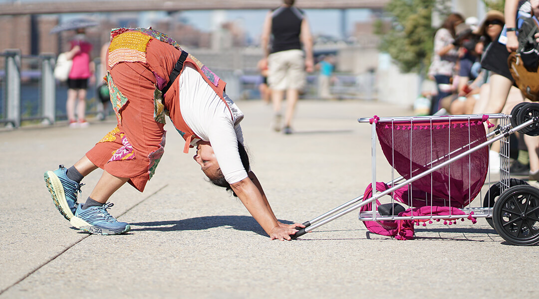 A person bent at the waist with feet and hands on the ground in front of a tipped over small wheeled cart.