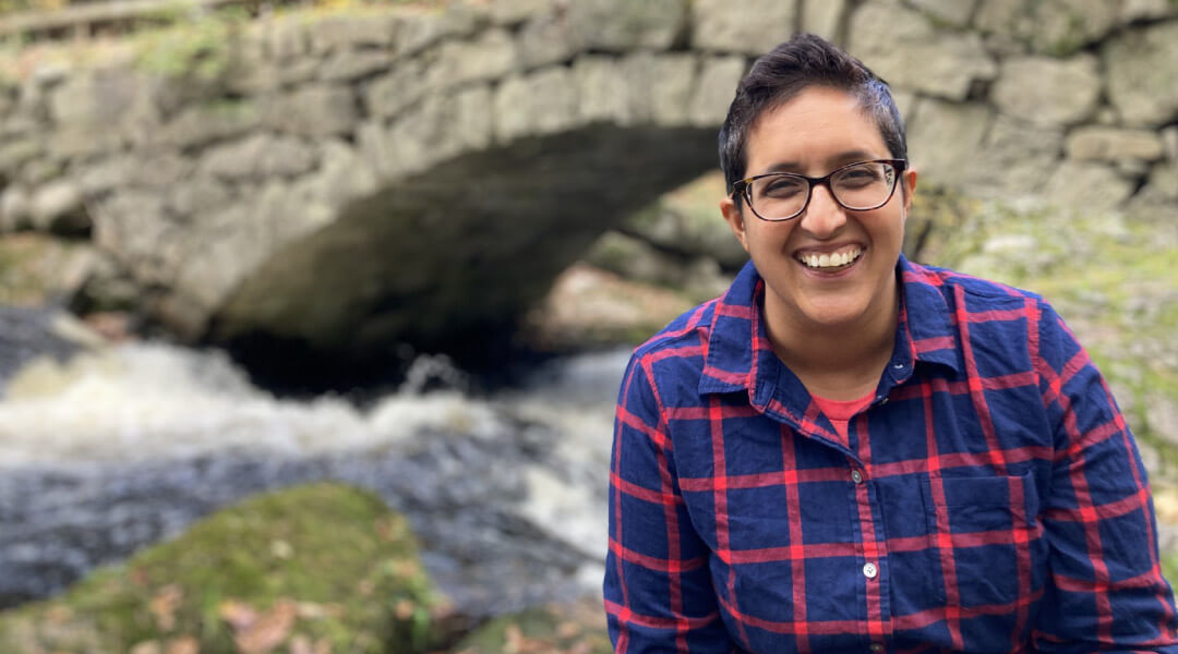 Photo of author Neema Avashia in front of a creek and stone bridge