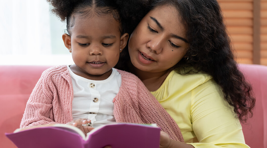 Adult and toddler reading a book together.